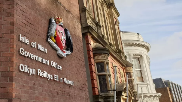 Isle of Man government offices, which has lettering on a red brick wall. The wedding cake Tynwald Building can be seen along side it.