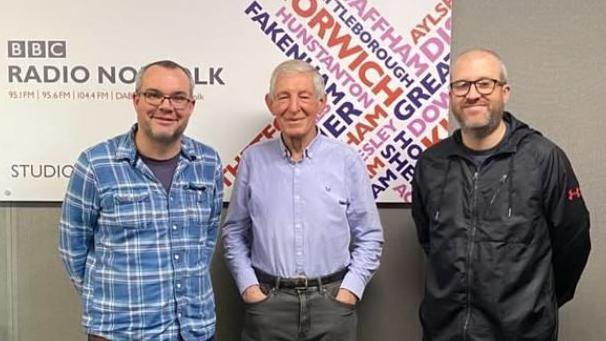 Chris Goreham, Gerry Harrison and Rob Butler stand in front of a BBC Radio Norfolk sign.