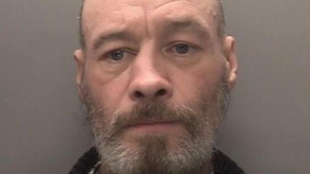 Mugshot of Alan Teague. He has bald head, and a grey and brown beard.