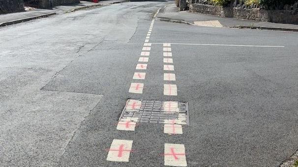 White give way markings at a junction with small red crosses spray painted on them.