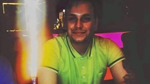 Lewis Skelton wearing a bright green polo shirt smiling into the camera with dimly lit neon surroundings