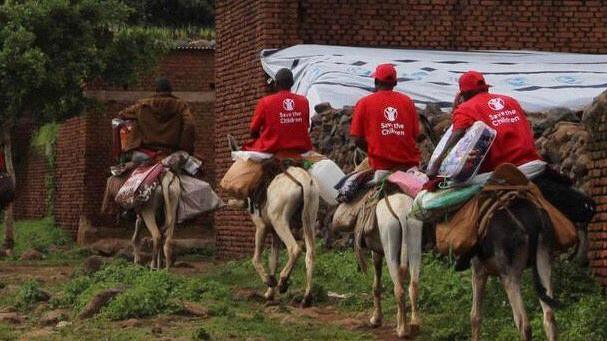 Aid workers in red T-shirts riding on donkeys carrying luggages down a hilly terrain