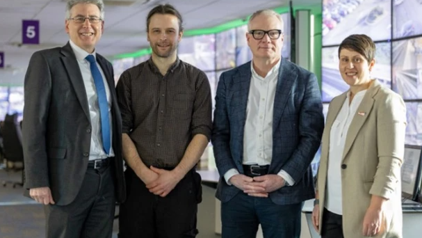 The four stand in a row inside an office and are smiling at the camera. The mayor and PCC are wearing dark suits, Mr McDonald is wearing a grey shirt and dark trousers, and Ms Marston has a beige jacket on over a white top an dark trousers.