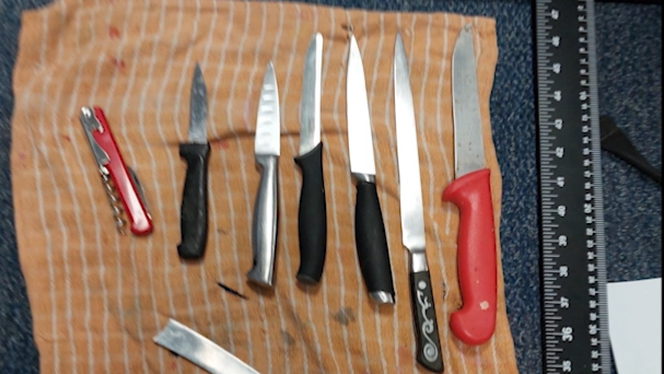 Seven knives of varying sizes lined up on a piece of orange and white stripy cloth.