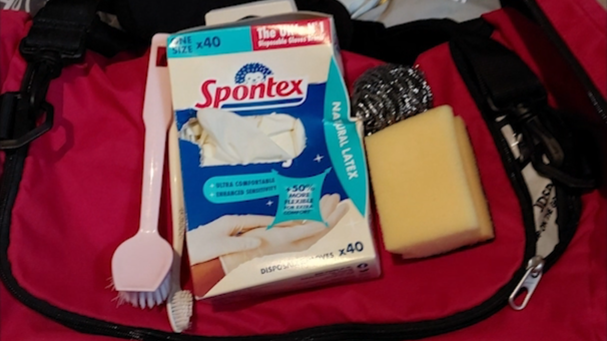 Cleaning supplies including a sponge, brushes and latex gloves on top of a pink bag. 