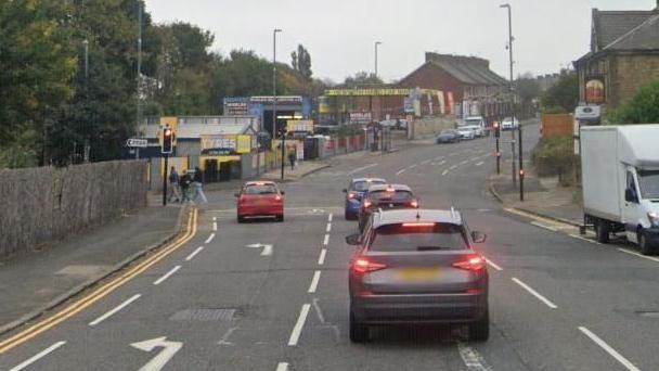 Google view of the B1426 Sunderland Road, near to the junction with Stoneygate Lane. Four cars have stopped at red traffic lights. Three pedestrians have just crossed the road.