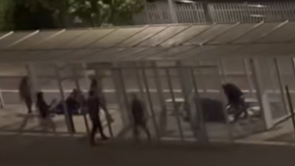 A grainy still from CCTV showing a group of people in dark clothes in a bus stop