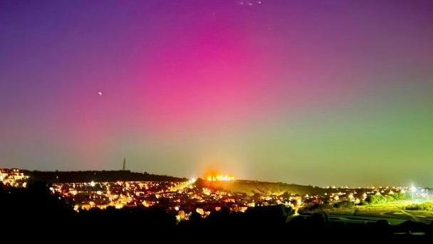 A pink and green sky above a city at night. 