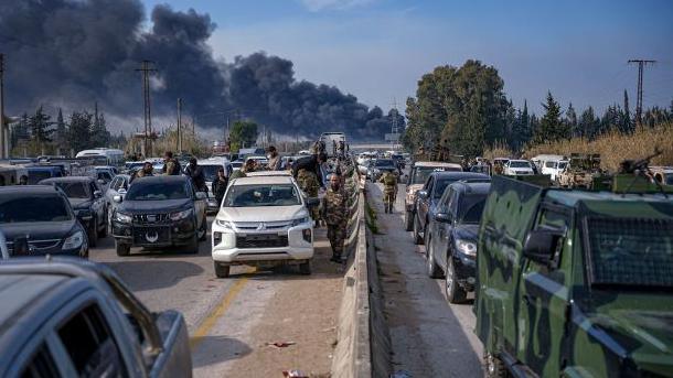 A line of military vehicles outside Latakia, Syria, with black plumes of smoke rising in the distance