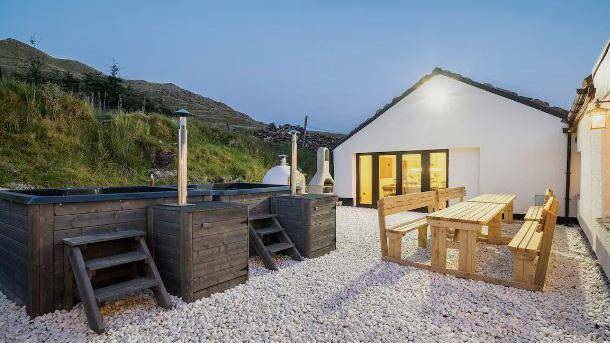 The external courtyard of one of the group accommodation blocks. It has two wooden hot tubs and woodfired ovens with picnic table and benches.