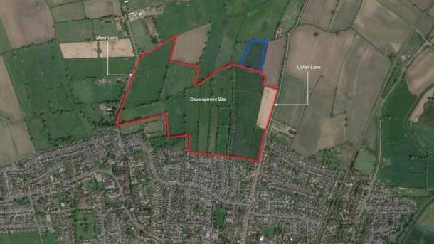 An aerial view of fields surrounding part of the villages of Haxby and Wiggington, with a red line marking out the circumference of the proposed development.