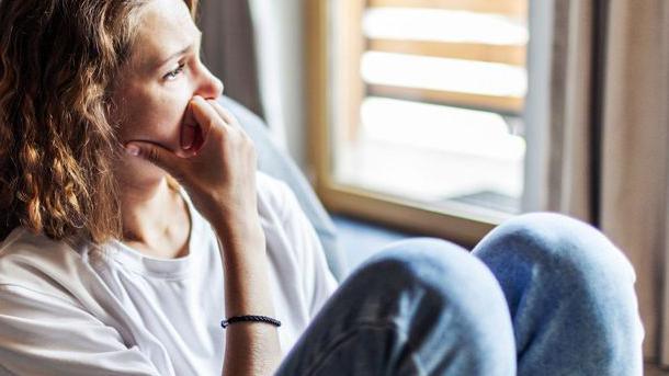 Woman looking pensive sitting on the floor with her back against a bed