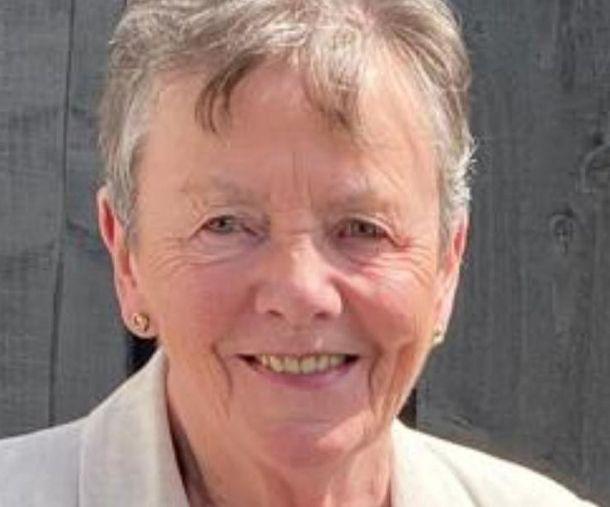 A woman with short greying hair in a white jacket, smiling at the camera