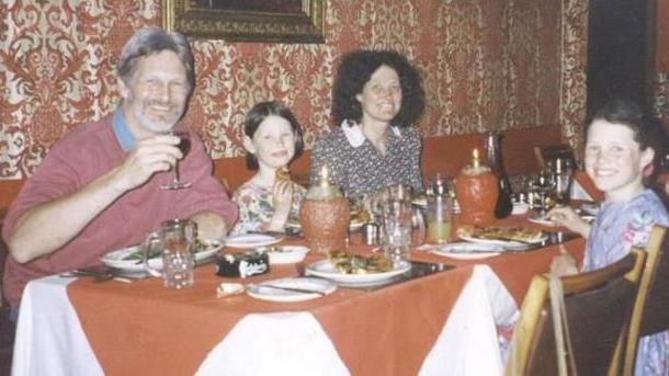 A meal  array  with orangish  array  cloth and candles and plates of food. A grey-haired man, brunette pistillate   and 2  young brunette girls are sat astir   the table. They are smiling and looking astatine  the camera.
