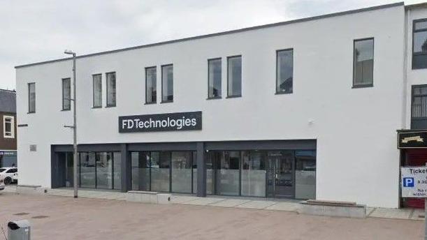 A white building with ten rectangular glass windows. The building has glass doors and a black sign that says FD technologies in white writing.