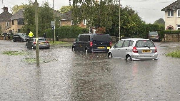 Three cars submerged in water halfway up their wheels on a road in Oxford