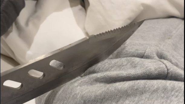 A silver knife lying on grey tracksuit material. A line of three holes are visible in the knife blade.