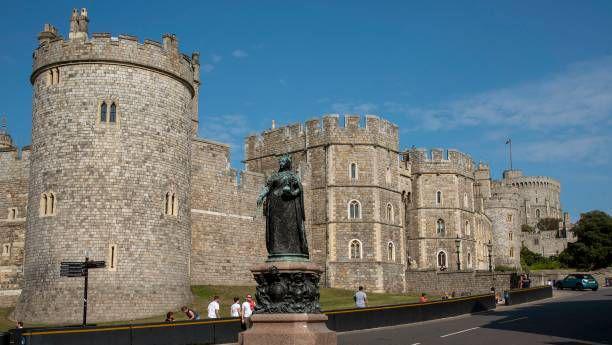 Shot of the road outside the main entrance to Windsor Castle with the statue of Queen Victoria in the foreground and the Castle behind her with a bright sky above.