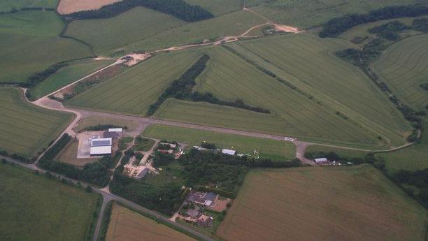 An aerial shot of Spanhoe airfield showing concrete runways and two hangar-like buildings, plus woods and other buildings, set among fields