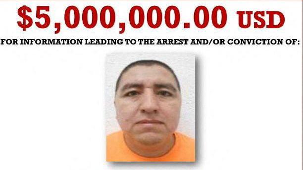 A screengrab of a Wanted poster shows a mugshot of Flores wearing an orange T-shirt. The text above his photo reads: $5,000,000.00 USD for information leading to the arrest and/or conviction of: