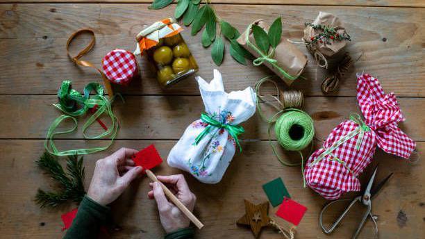 An assortment of festive-looking jars and small gifts on a wooden table wrapped in reuseable linen coverings, green twine and brown paper