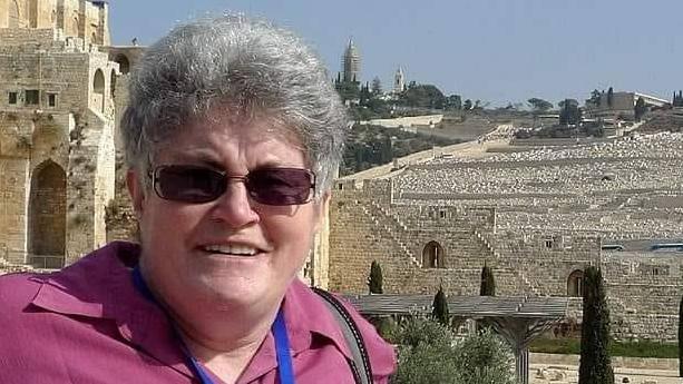 Davinia Graham, wearing a pink shirt, standing outside an ancient site with old buildings