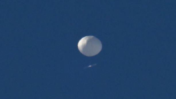 A Chinese spy balloon, white and indistinct as it is far away, against a deep blue sky.
