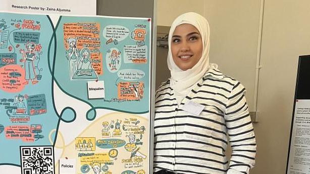 Llun o Zaina yn gwneud cyflwyniad, maen gwisgo hijab a thop streipiog.