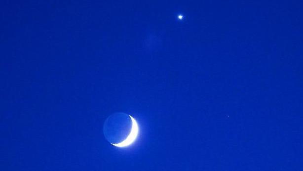 A crescent moon and Venus against a royal blue sky