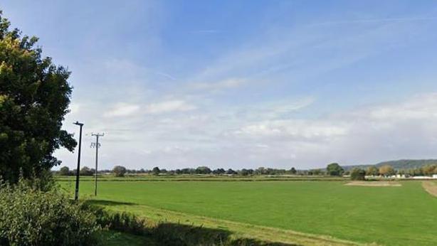 A green field with telephone pylons underneath a clouded sky