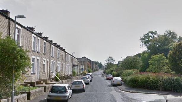 A road view of Southfield Street in Nelson, houses are on the left with parked cars and a park is on the right with two parked cars, it is a narrow road