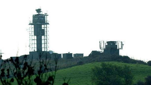 Two watch towers on top of a green mound on a grey day with trees at the front of the shot.