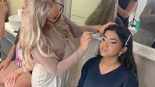 A girl having her makeup done by the co-owner of the salon