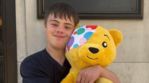 A man with brown hair smiling and hugging a Pudsey toy.