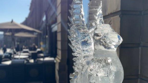 An ice figure of a bird on the street. The outdoor seating area of a bar is in the background.