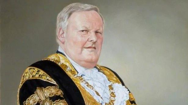 A portrait of former Belfast Lord Mayor Lord Wallace Browne - he is pictured wearing a traditional black and gold robe with white ruffle details