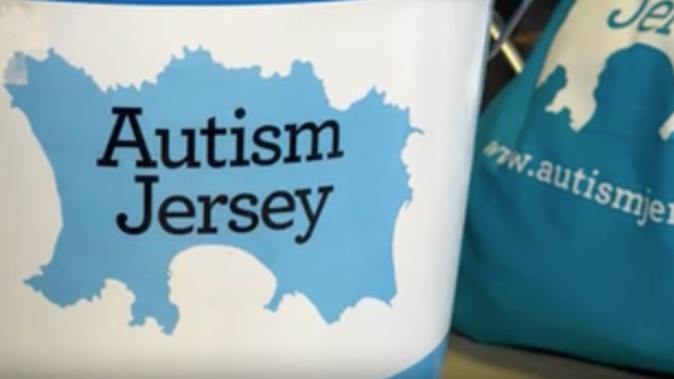 The Autism Jersey logo - the title over a blue sketch of the island - on a white cover on a blue bucket. A blue Autism Jersey bag in next to it on a desk.