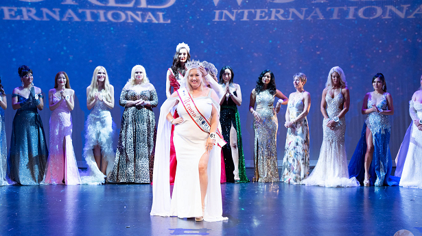 A woman wearing a white wedding dress stands in front of a line up of women