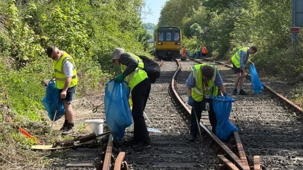 Volunteers in hi-vis vest litter pick along a railway track