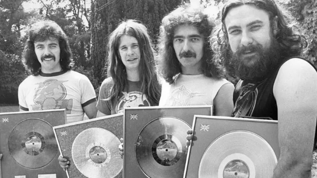 Four men holding records looking into the camera smiling. 