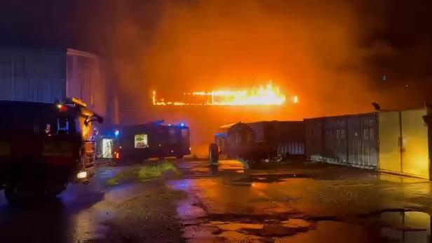 Large blaze at industrial unit in distance with fire engines in the foreground