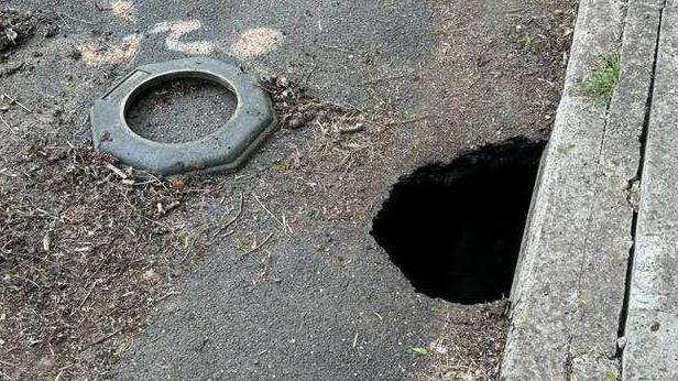 A road in Castle Cary, Somerset, with a hole on the side of the road right next to the pavement.