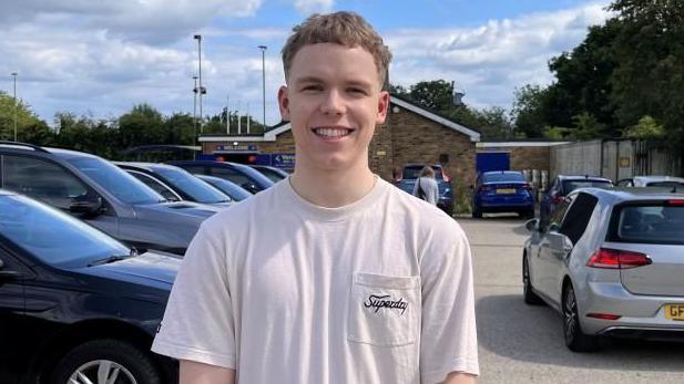 Alex Russell in a white t-shirt standing in a car park