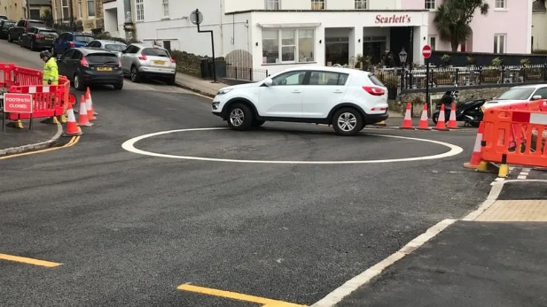 A car in the middle of a large white circle painted on a road