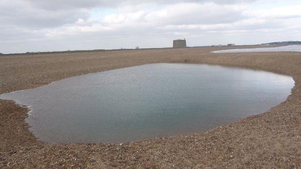 A hole on a beach, filled with water.