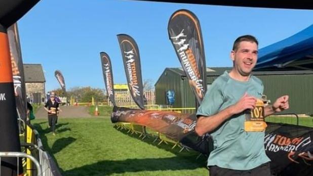 Picture shows Kieron crossing the finishing line of a 'tough runner' event 