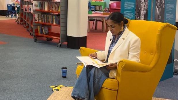 Ellisha Soanes sits in a chair with a book in Ipswich County library.