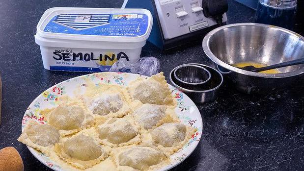 A plate is full of hand made ravioli made by one of the 2024 contestants. There is a box marked semolina and a mixing bowl with an egg mixture and spatula in it, beside some cutting shapes.