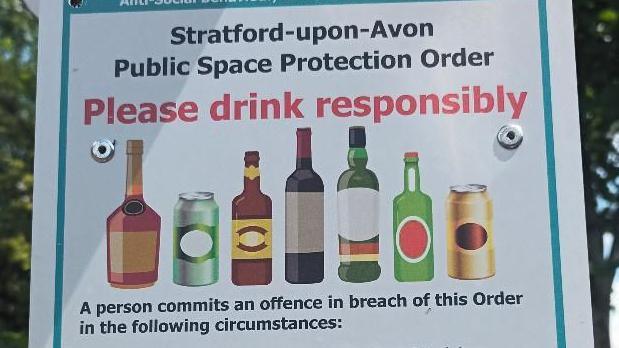 A white sign with red and black text reading Please drink responsibly , images of varying size bottles and cans are also shown.