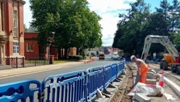 Blue fencing separates the middle of a road, with workers on side digging up the road and finding old rusted tramlines.
